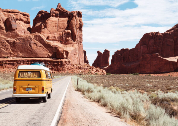 Ein kleines, gelbes Wohnmobil fährt entlang roter Felsen